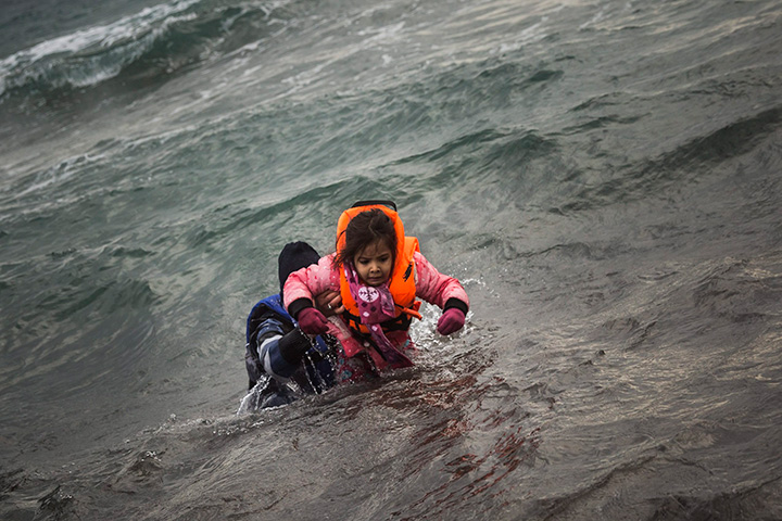 A man carries a child as they try to reach the shore after falling into the sea while disembarking from a dinghy on which they crossed a part of the Aegean Sea with other refugees and migrants, from Turkey to the Greek island of Lesbos, on Sunday, Jan. 3, 2016. 