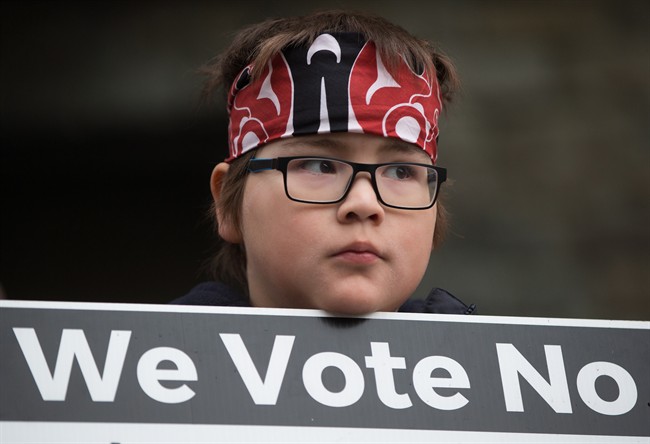 Jamie Antone, 9, of the Squamish First Nation, holds a sign as protesters gather outside National Energy Board hearings on the proposed Trans Mountain pipeline expansion in Burnaby, B.C., on Tuesday January 19, 2016. 