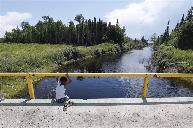 A boy from the Shoal Lake 40 First Nation sits on a bridge over a channel in this file photo.
