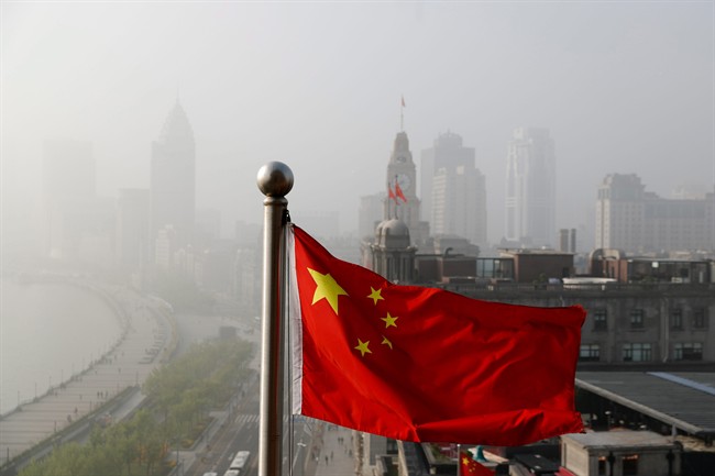 FILE - A Chinese national flag flutters against the office buildings at the Shanghai Bund shrouded by pollution and fog in Shanghai, China, Thursday, April 14, 2016.