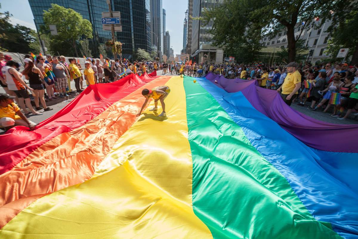 Revelers spread out a giant LGBT flag in the streets of Montreal during the Montreal Pride parade on August 16, 2015.