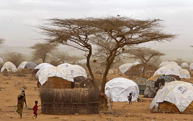 Refugees walk amongst huts at a refugee camp in Dadaab, Kenya. Kenya's interior minister said Wednesday, May 11, 2016 that the government will close Dadaab refugee camp which has hundreds of thousands of Somali refugees and is often referred to as the world's largest refugee camp. 