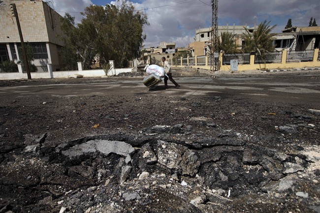 In this Thursday, April 14, 2016 photo, a Syrian man pushes a trolley with his belongings to load them onto a bus with others leaving their home towns, near a crater in the town of Palmyra in the central Homs province, Syria. 