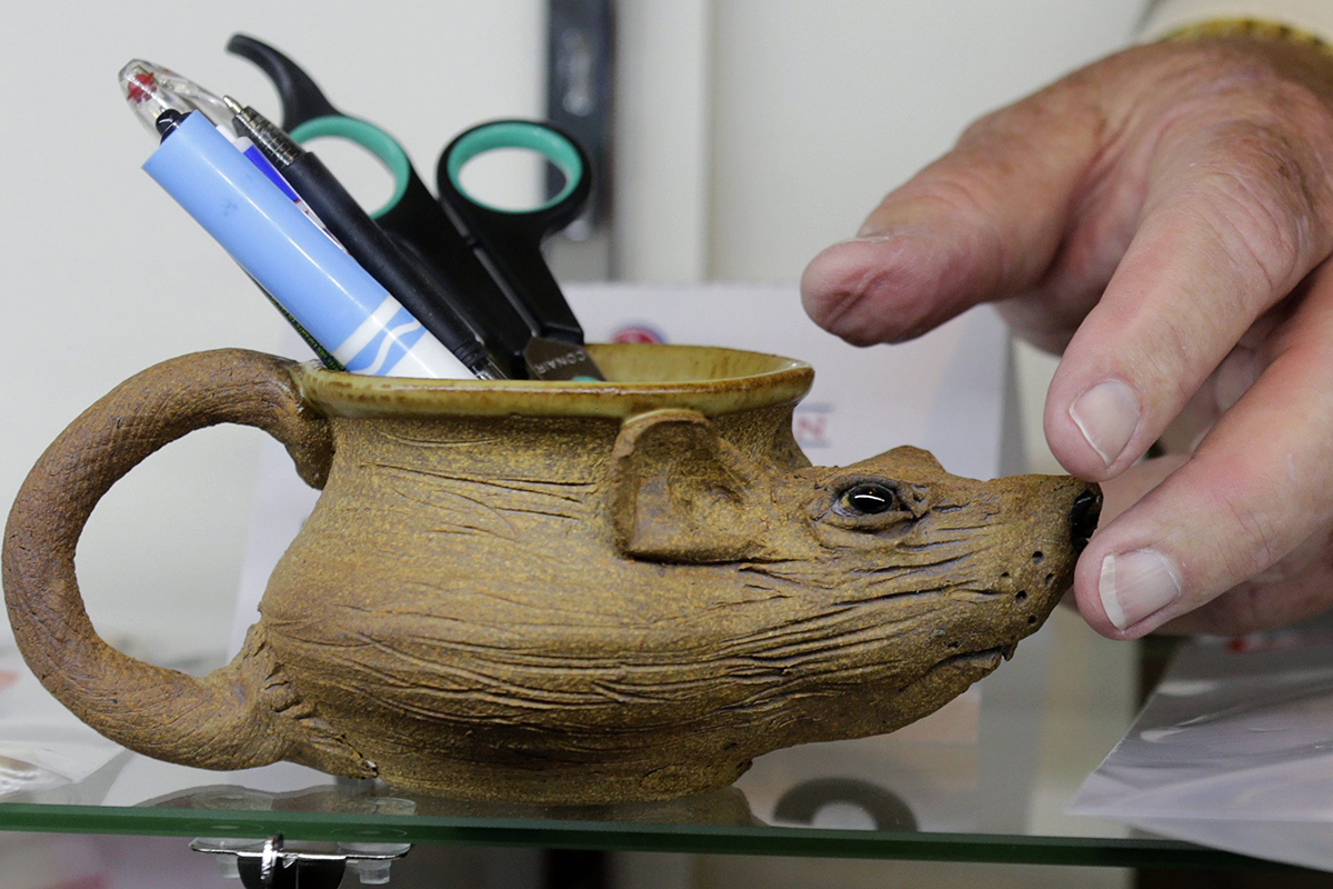 Auctioneer Bob Sheehan reaches for a pottery mug, in the shape of a rat, which contains pens, that are among items belonging to James "Whitey" Bulger and Catherine Greig.