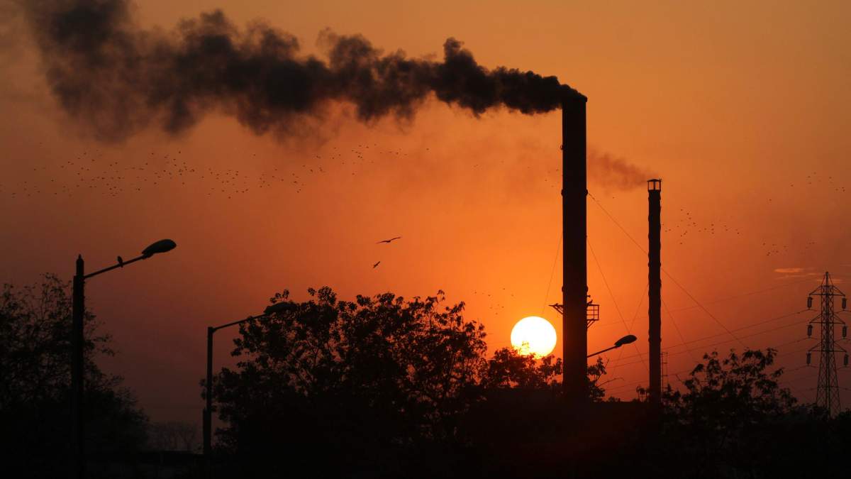 FILE - This is a Monday, Dec. 8, 2014 file photo of birds as they fly past at sunset as smoke emits from a chimney at a factory in Ahmadabad, India.