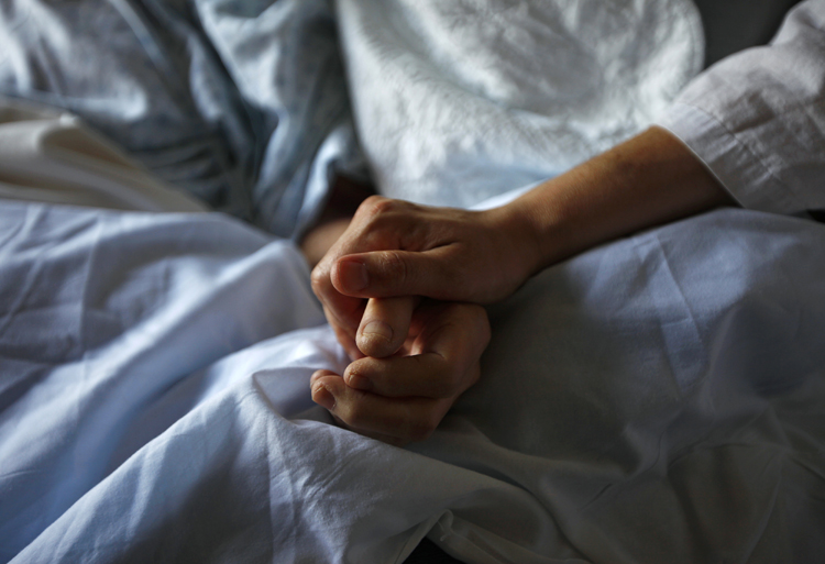 A woman holds the hand of her mother who is dying from cancer during her final hours at a palliative care hospital in Winnipeg in this image from 2010. 