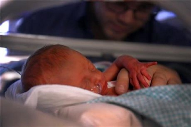 First-born of the triplets, Raelyn stretches in her isolette while her father Logan Fletcher holds her.