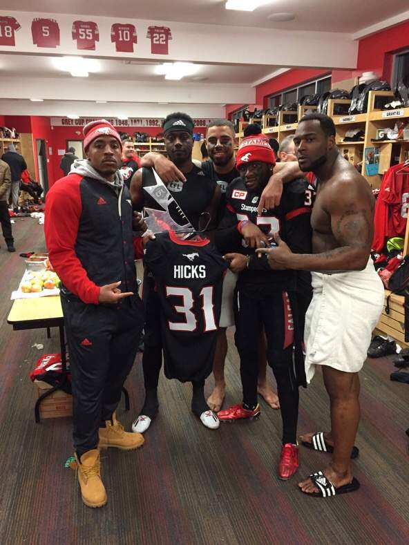 A few of the Calgary Stampeders players hold up Mylan Hicks jersey in the locker room ahead of the 104th Grey Cup.