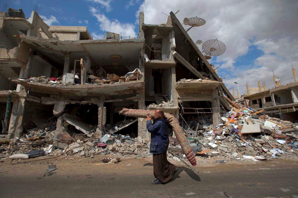 A Syrian man carries a carpet as he walks through a devastated section of the ancient town of Palmyra in this April 14, 2016 file photo.



