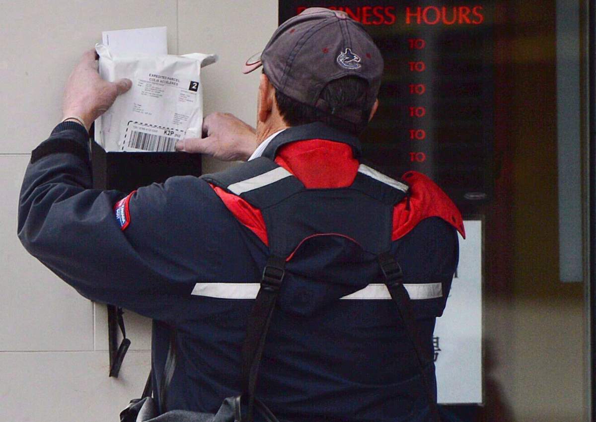 A mail carrier delivers mail in Ottawa, on Dec.11, 2013. A House of Commons committee is recommending Canada Post come up with a plan to reinstate door-to-door delivery in parts of the country that lost the service in the last year and maintain a freeze on the installation of community mailboxes.