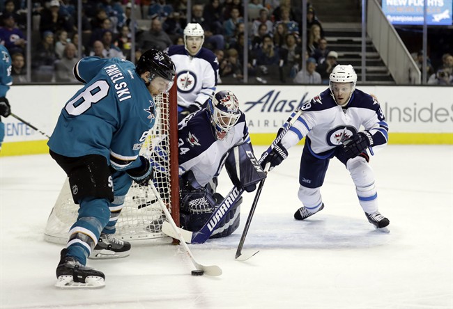 San Jose Sharks' Joe Pavelski (8) controls the puck in front of Winnipeg Jets goalie Michael Hutchinson (34) and Toby Enstrom, right, during the second period of an NHL hockey game, Monday, Jan. 16, 2017, in San Jose, Calif.