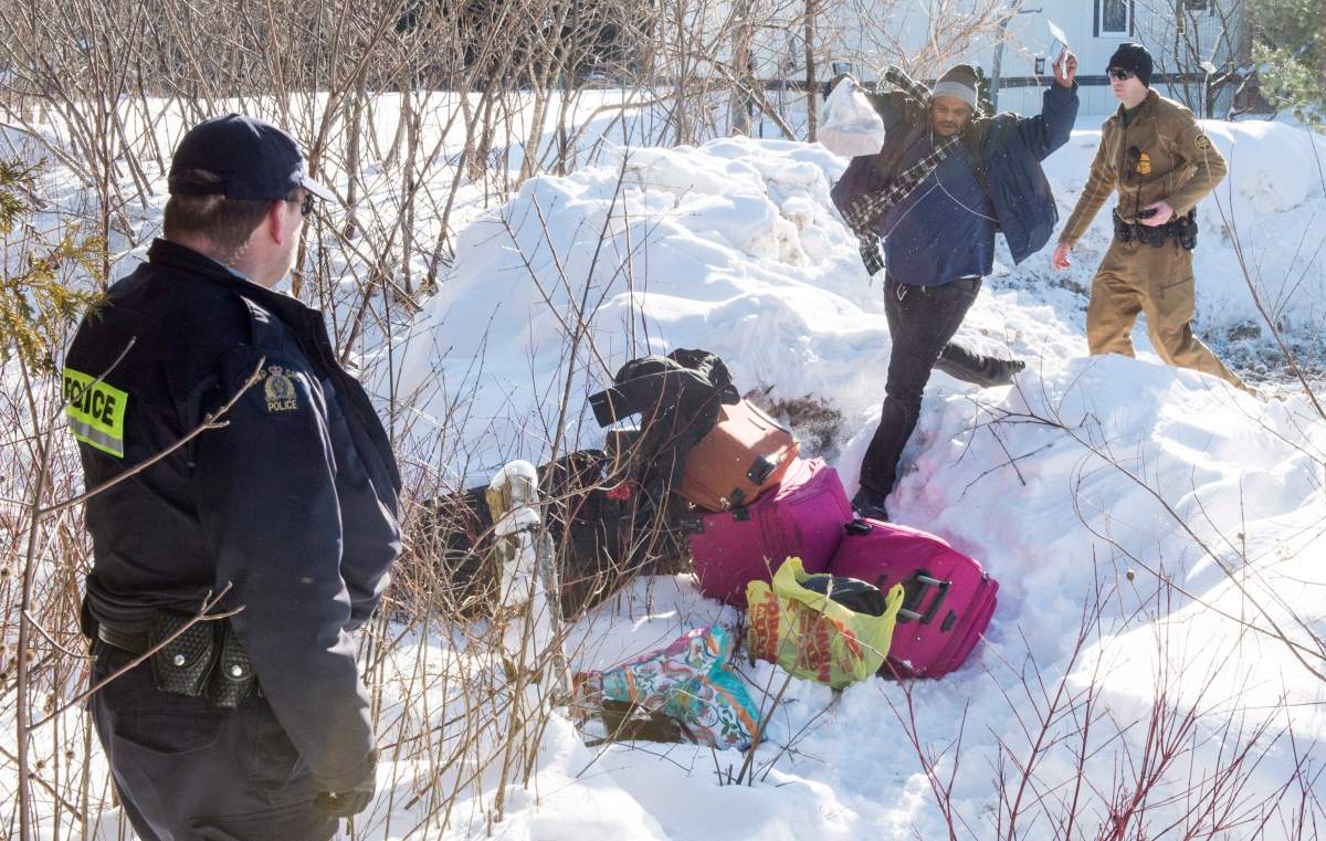 A Somali man leaps across the border between an RCMP officer and a U.S. Border Patrol agent at the U.S.-Canada border near Hemmingford, Que., on Friday, Feb. 17, 2017. A number of refugee claimants are braving the elements to illicitly enter Canada.