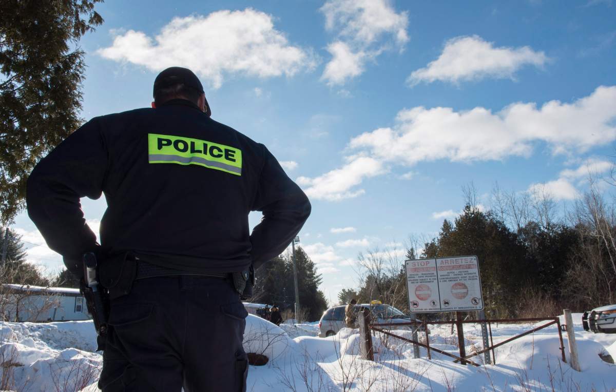 An RCMP officer looks on as two Somali families prepare to cross the U.S.-Canada border near Hemmingford, Que., on Friday, Feb. 17, 2017. A number of refugee claimants are braving the elements to illicitly enter Canada.