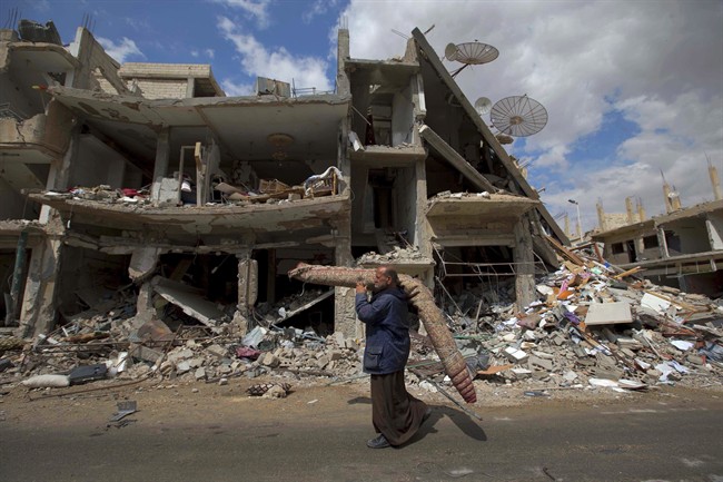 In this April 14, 2016 file photo, a Syrian man carries a carpet through a devastated part of the town of Palmyra as families load their belongings onto buses in the central Homs province in Syria. 
