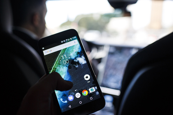 The Uber Technologies Inc. ride-hailing service app sits on a smartphone screen in the rear of an Uber Technologies Tesla Motors Inc. Model S electric automobile, in Madrid, Spain, on Friday, Jan. 13, 2017. Ride-hailing service Uber Technologies has launched its first electric car taxi service in Madrid, operating a fleet of Tesla Model S electric vehicles. Photographer: Angel Navarrete/Bloomberg via Getty Images.