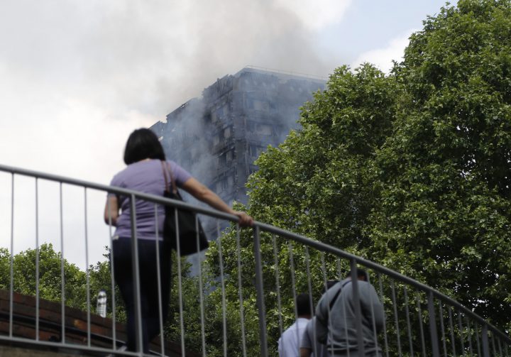The high-rise apartment building where a massive fire raged smoulders as people cross a pedestrian bridge nearby, in London, June 14, 2017.