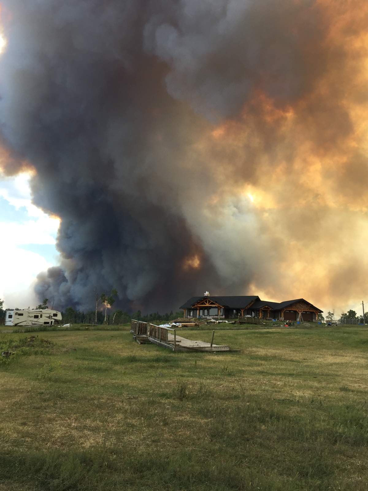 Thick smoke fills the sky as the forest burns behind a home near 100 Mile House.