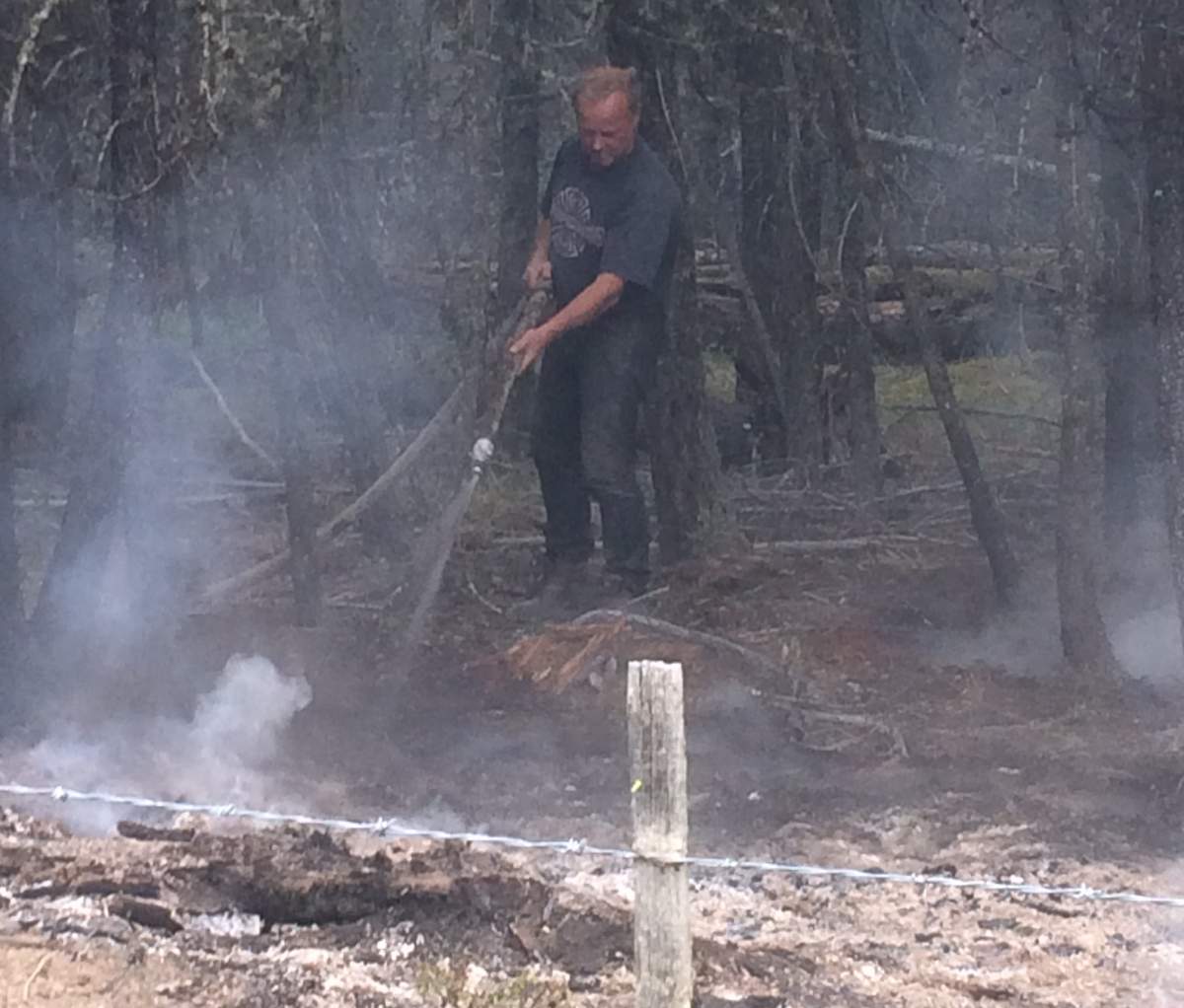 A rancher uses a hose to put out hotspots by a home near 100 Mile House.