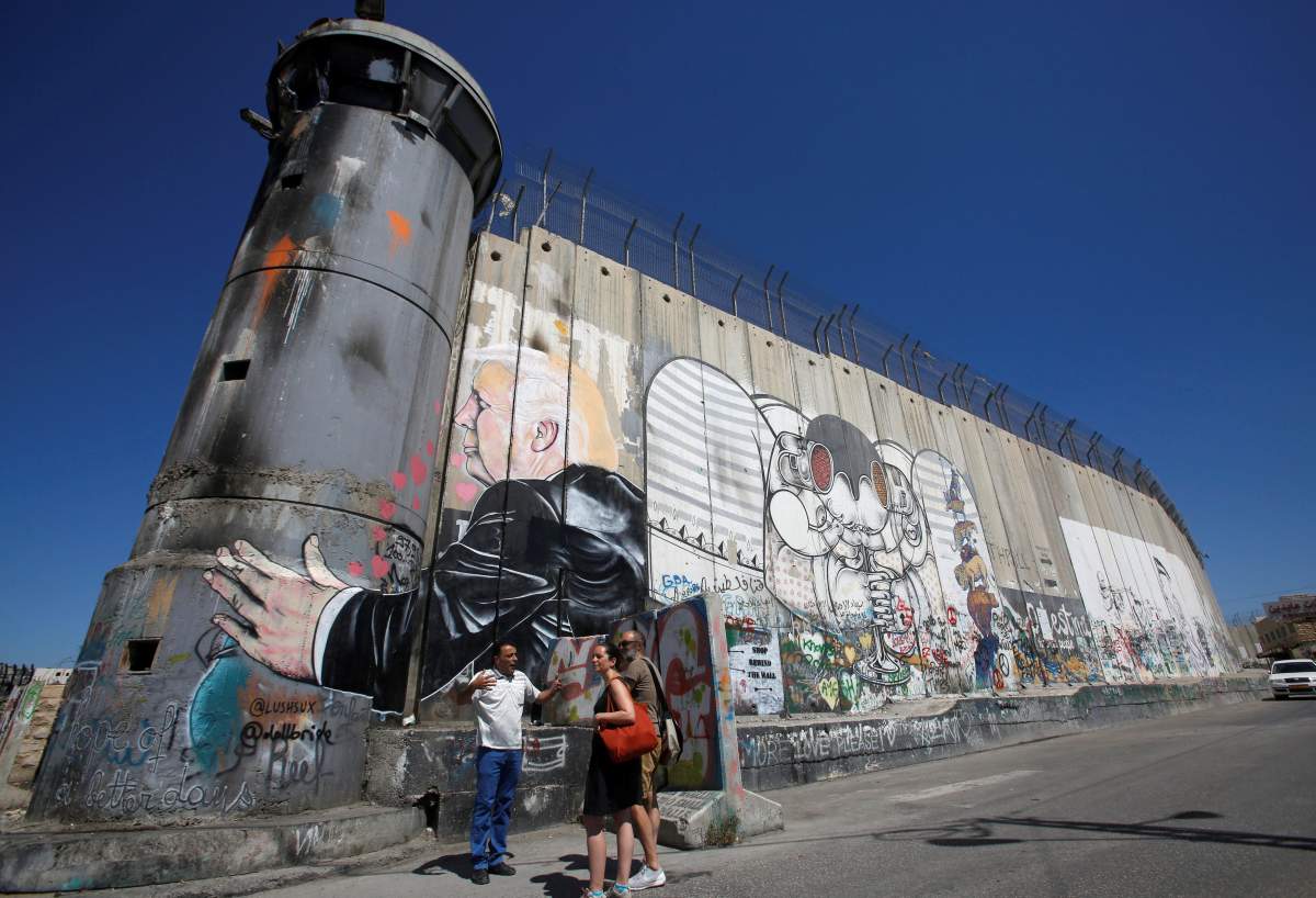 Tourists stand in front of a graffiti depicting U.S President Donald Trump on the controversial Israeli barrier in the West Bank town of Bethlehem August 4, 2017.