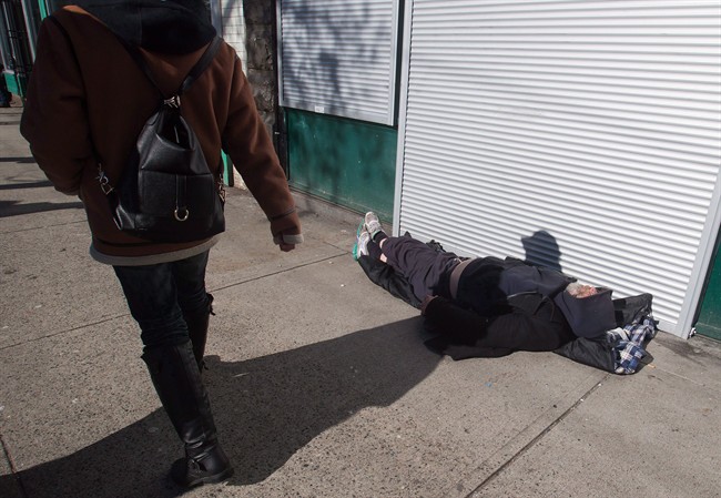 A woman walks past a man sleeping on the street in the Downtown Eastside of Vancouver, B.C., on Tuesday, February 21, 2017.