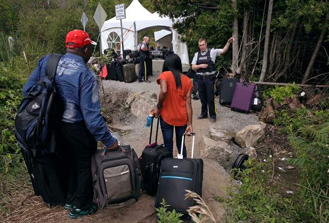 A Royal Canadian Mounted Police officer informs a migrant couple of the location of a legal border station, shortly before they illegally crossing from Champlain, N.Y., to Saint-Bernard-de-Lacolle, Quebec, Monday, Aug. 7, 2017. (AP Photo/Charles Krupa).