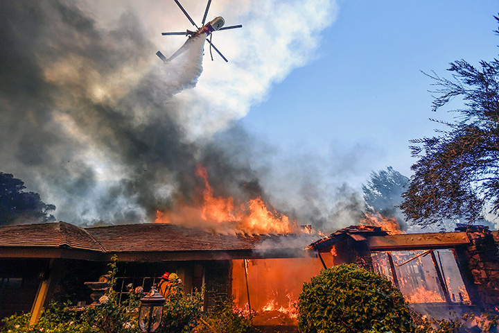A helicopter dumps water on a home as firefighters battle a wildfire in Anaheim Hills, California, Monday, Oct. 9, 2017.