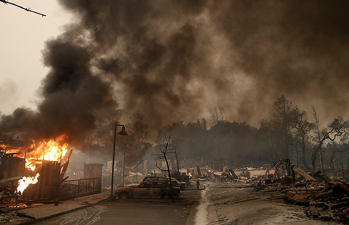 Burned out cars sit next to a building on fire in Santa Rosa, California on October 9, 2017.