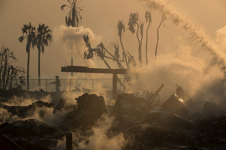 A firefighter sprays water on the remains of the Hawaiian Village apartments after a wind-driven wildfire swept into the city of Ventura, California, December 5, 2017.