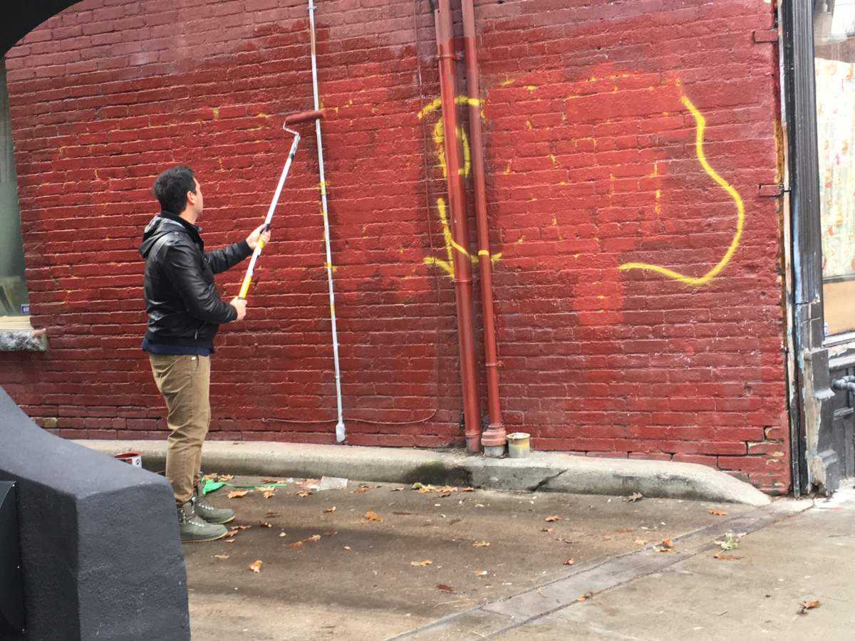 Photographer George Pimentel paints over a tag spray painted on the wall of the bar neighbouring his studio.