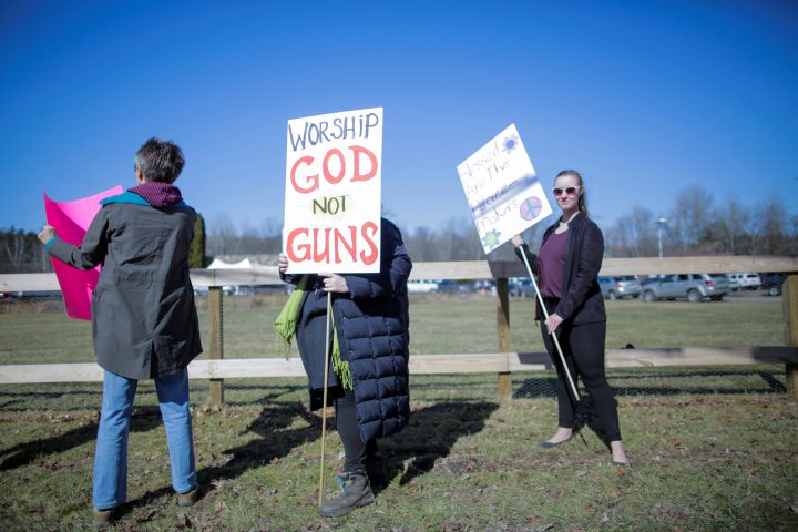 People protest outside the church as worshipers attend a blessing ceremony with their AR-15-style rifles.