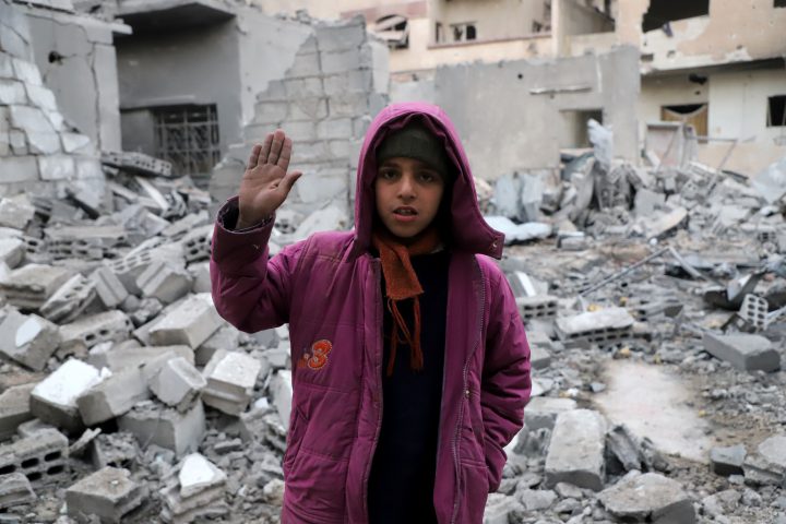 A Syrian girl raises her hand as she poses for a photo.