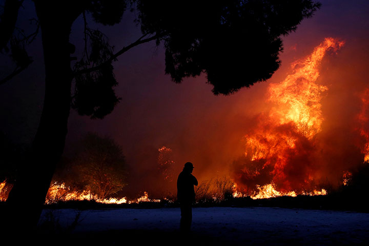 A man looks at the flames as a wildfire burns in the town of Rafina, near Athens, Greece, July 23, 2018.