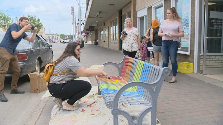 In a July 2018 photo, community members of Moose Jaw Pride invited the community paint the bench outside of Rainbow Retro Thrift Shop with Pride colours.