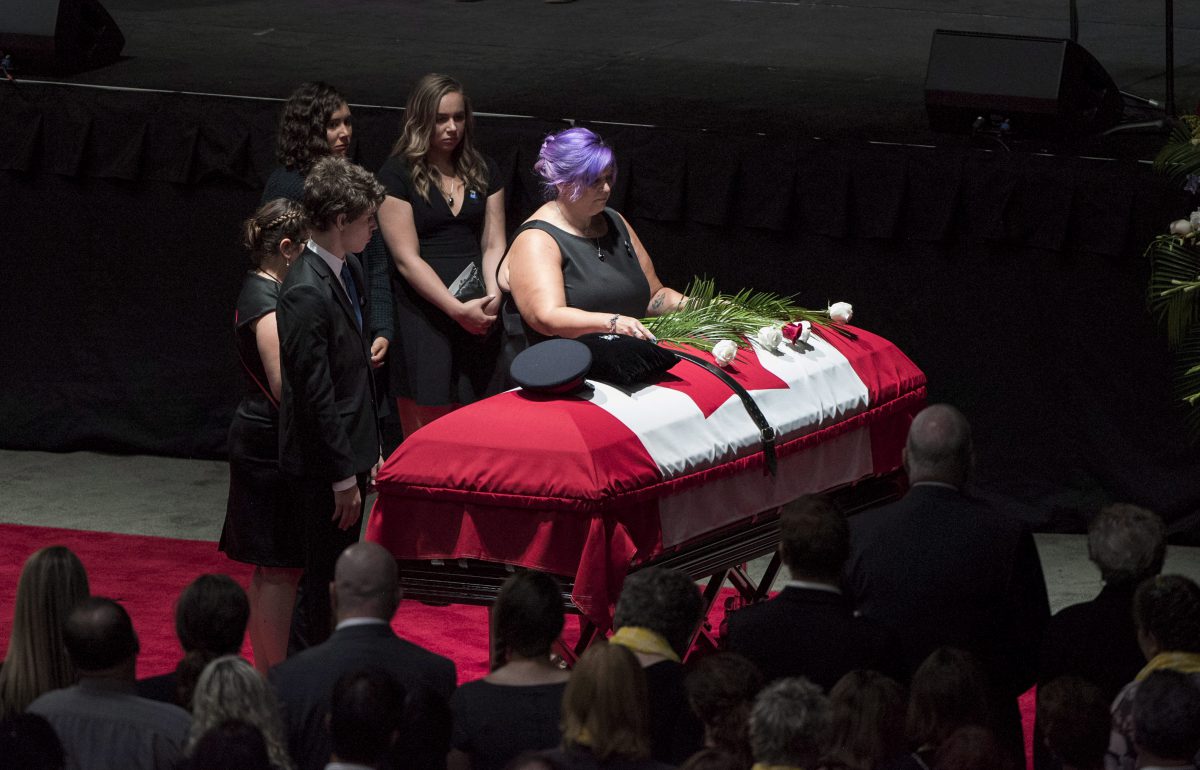 Jackie McLean lays a flower on the flag-draped casket of her slain husband Fredericton police officer Cst. Robb Costello as their children stand by during a regimental funeral for Cst. Costello and Cst. Sara Burns in Fredericton on Saturday, August 18, 2018.