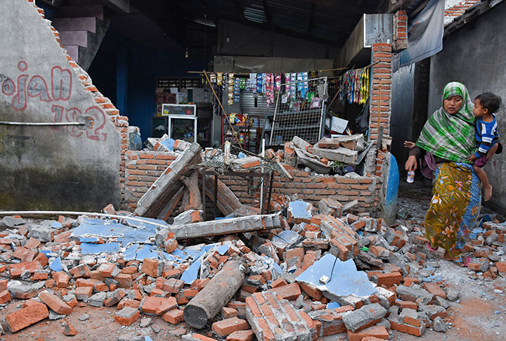 A woman walks past debris from a collapsed wall following a strong earthquake in Lendang Bajur Hamlet, Lombok island, Indonesia August 6, 2018.