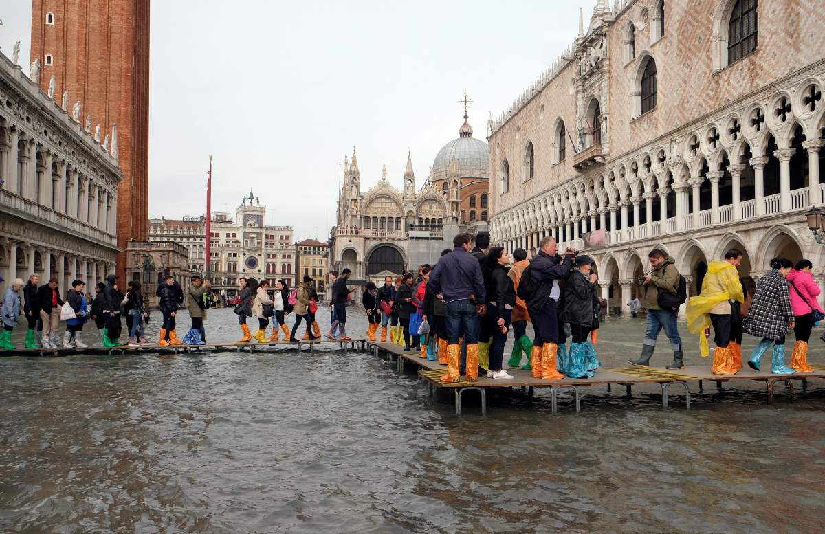 People walk on a catwalk in a flooded Saint Mark Square during a period of seasonal high water in Venice, Italy October 29, 2018.