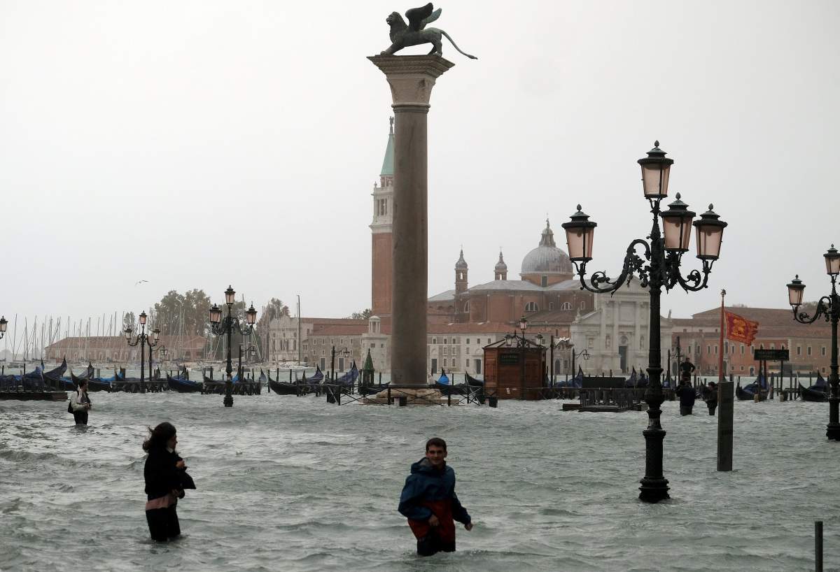 People walk in flooded Saint Mark Square during a period of seasonal high water in Venice, Italy October 29, 2018.