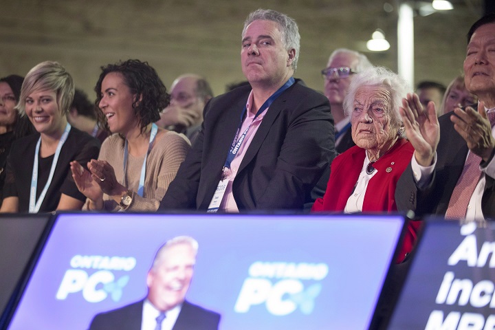 Dean French (centre) chief of staff for Doug Ford, listens to the Ontario Premier, pictured on a monitor, speak at the Ontario PC Convention in Toronto, on Friday.