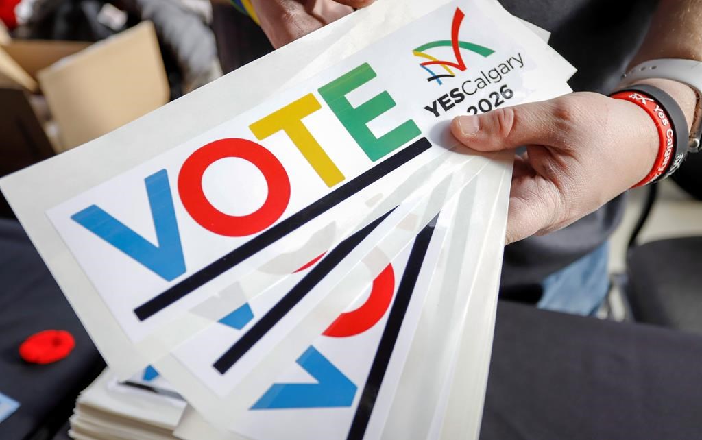 Bumper stickers are handed out during a rally in support of the 2026 Winter Olympic bid in Calgary on Nov. 5, 2018. The city ended up deciding against submitting an official bid after more than 56 per cent of voters rejected the idea in a public plebiscite.