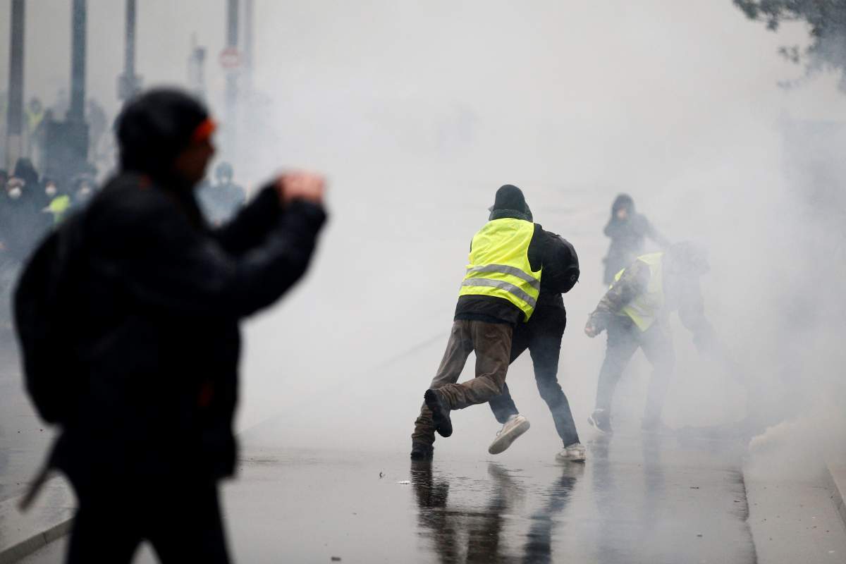 A man wearing a yellow vest tackles a protester as tear gas floats in the air during clashes with police at a demonstration by the “yellow vests” movement in Nantes, France, December 15, 2018.