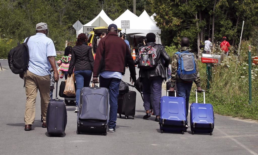 A family from Haiti approaches a tent in Saint-Bernard-de-Lacolle, Que., as they haul their luggage down Roxham Road in Champlain, N.Y., Aug. 7, 2017. THE CANADIAN PRESS/AP-Charles Krupa