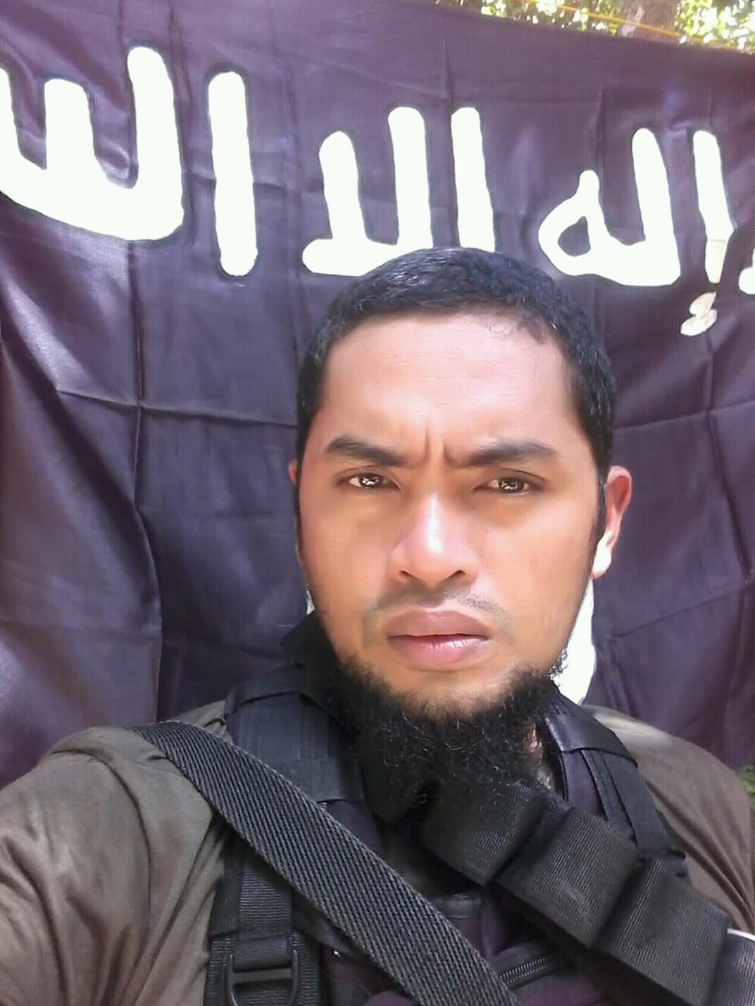 Facebook photo of Behn Tatuh, with ISIS flag behind him.
