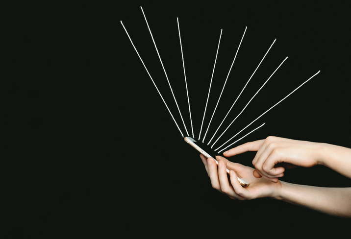 Hand holding a mobile phone, white yarn beams radiating from the phone.