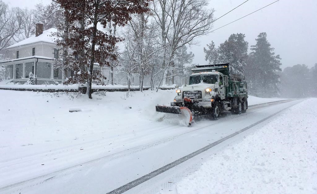 A snow plow moves snow on a wintery street.
