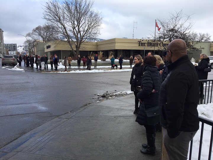 People stand on opposite corners from the Interior Health building at Doyle Avenue and St. Paul Street.