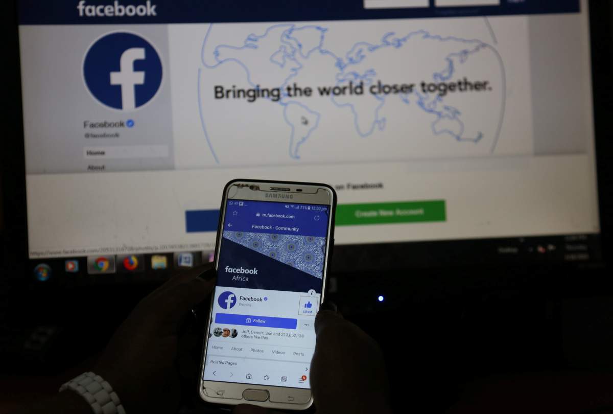 An illustration photo shows the Facebook page displayed on a mobile phone internet browser held in front of a computer screen.