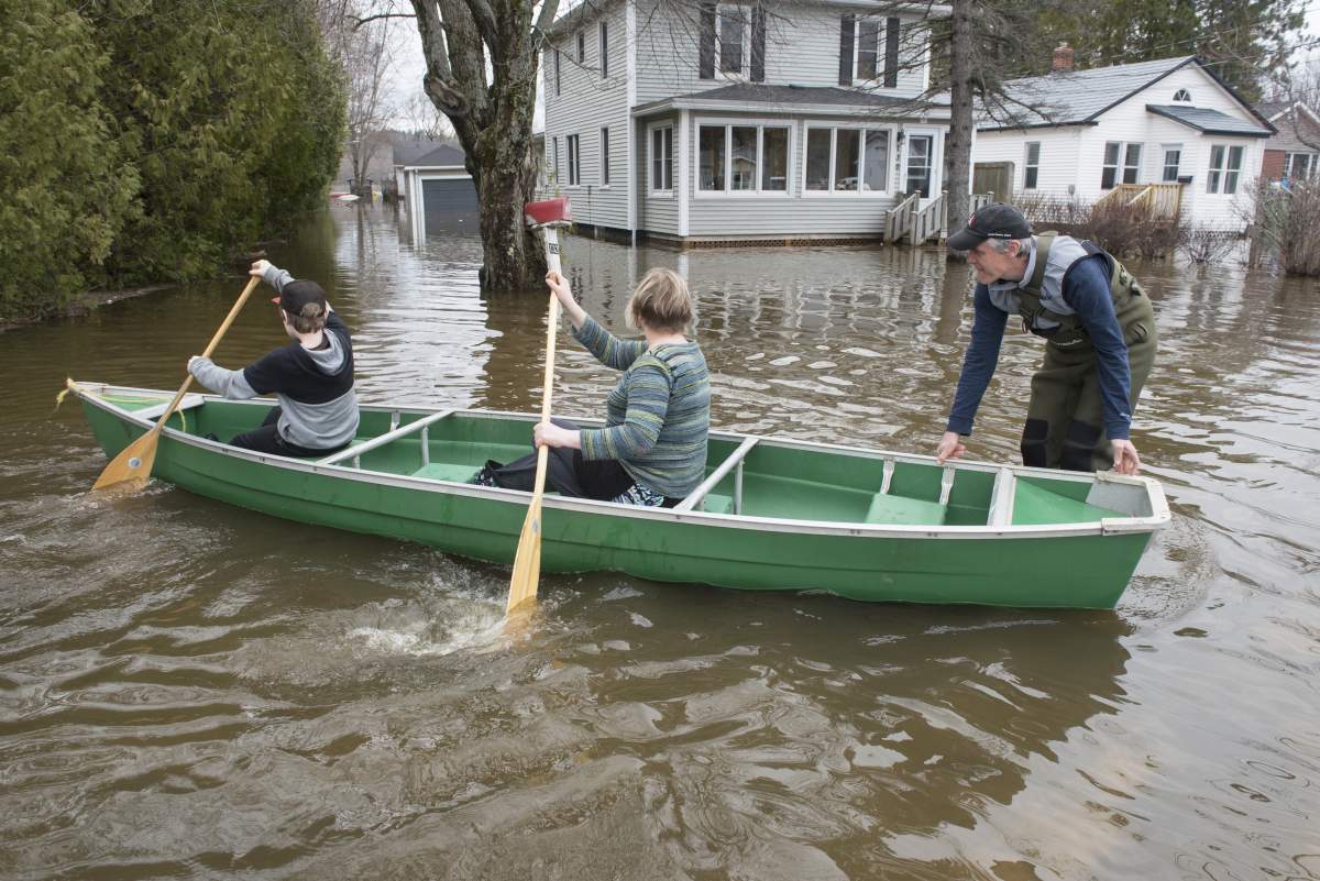 Peter Toner, right, Peta Fussell and their son Harry, 11, use a canoe and chest waders to check on their home on Riverside Drive in Fredericton on Monday April 22, 2019. THE CANADIAN PRESS/Stephen MacGillivray