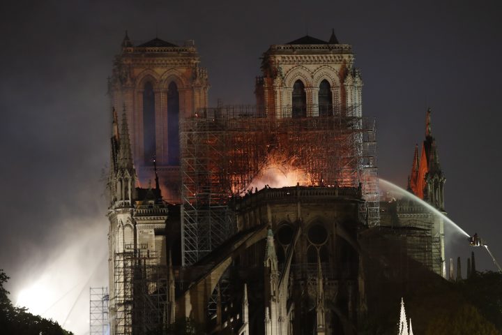 People watch Notre Dame cathedral burning in Paris, Monday, April 15, 2019. Flying buttresses can be seen connected to the structure at the bottom of the photo.