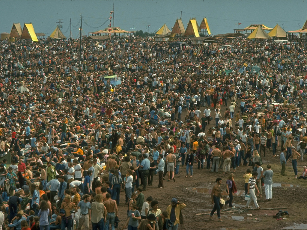 A huge crowd looking towards the large yellow tents during the Woodstock Music and Art Fair in 1969.