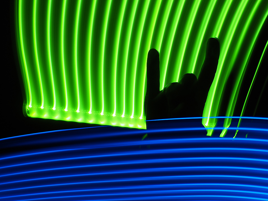 A person makes the "rock on!" sign with a neon light backdrop.